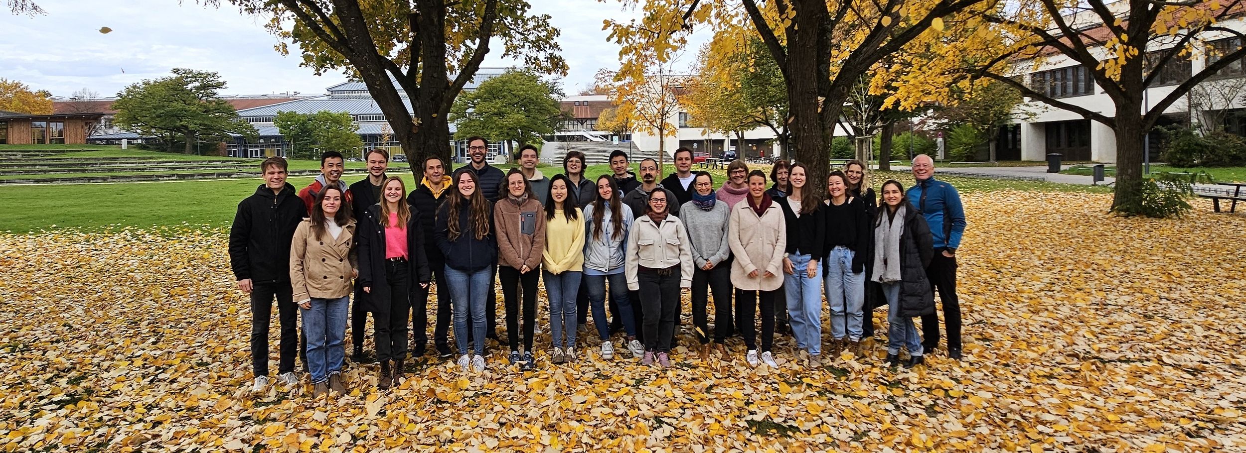 A group photo of about 25 people in front of trees in autumn